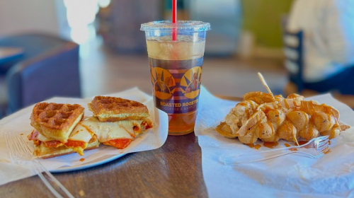 A plate with two waffle sandwiches and a drink on the side, set in a cozy café environment.